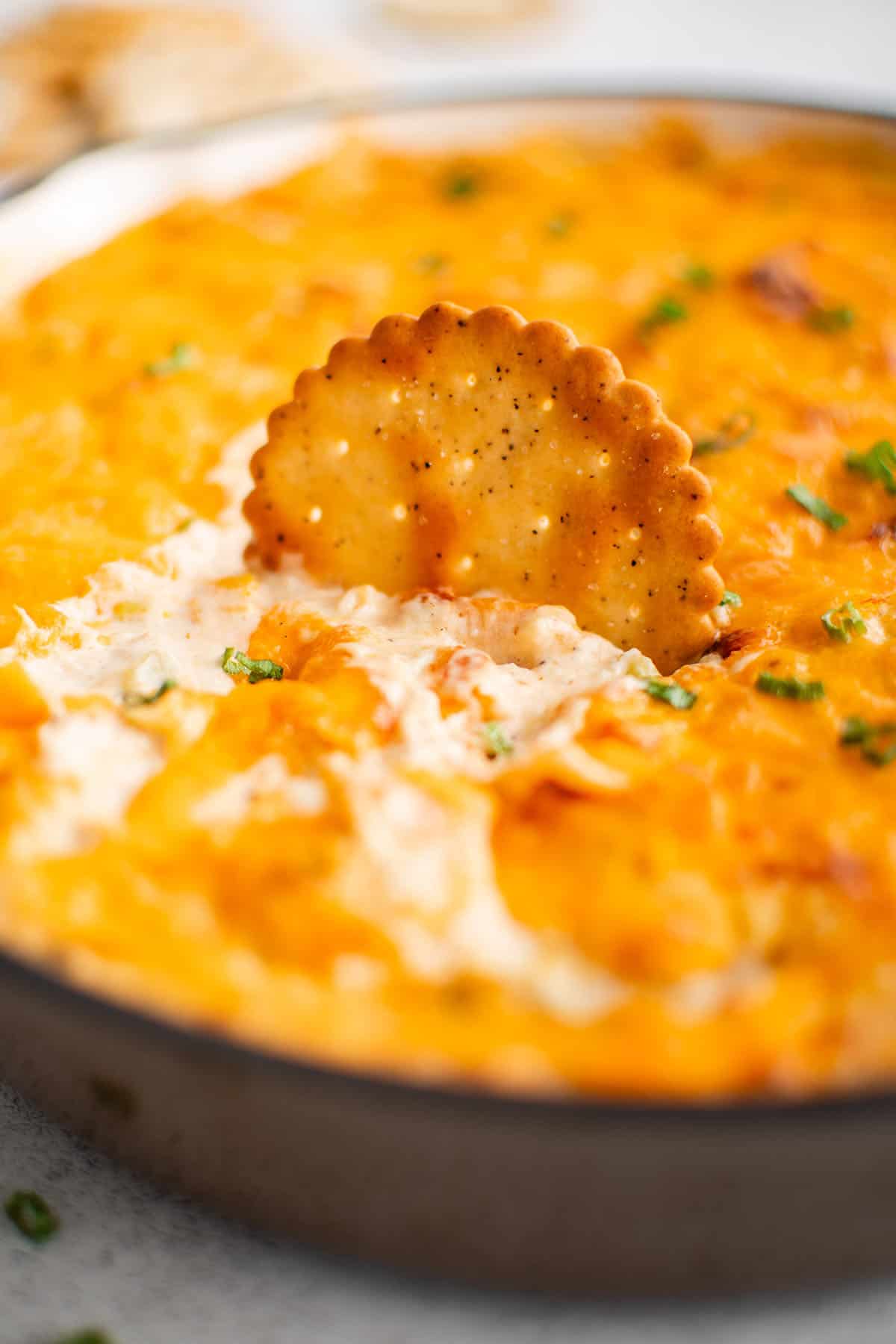 baked crab dip in a pan with a cracker